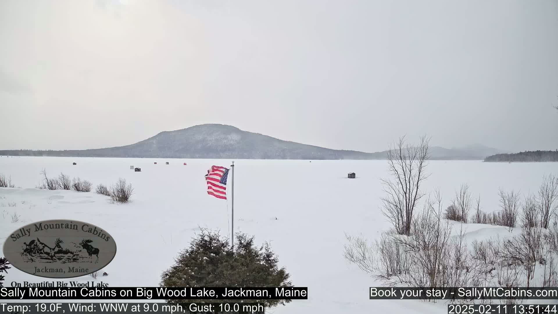 A snow-covered frozen lake stretches to a distant, snow-capped mountain under an overcast sky.