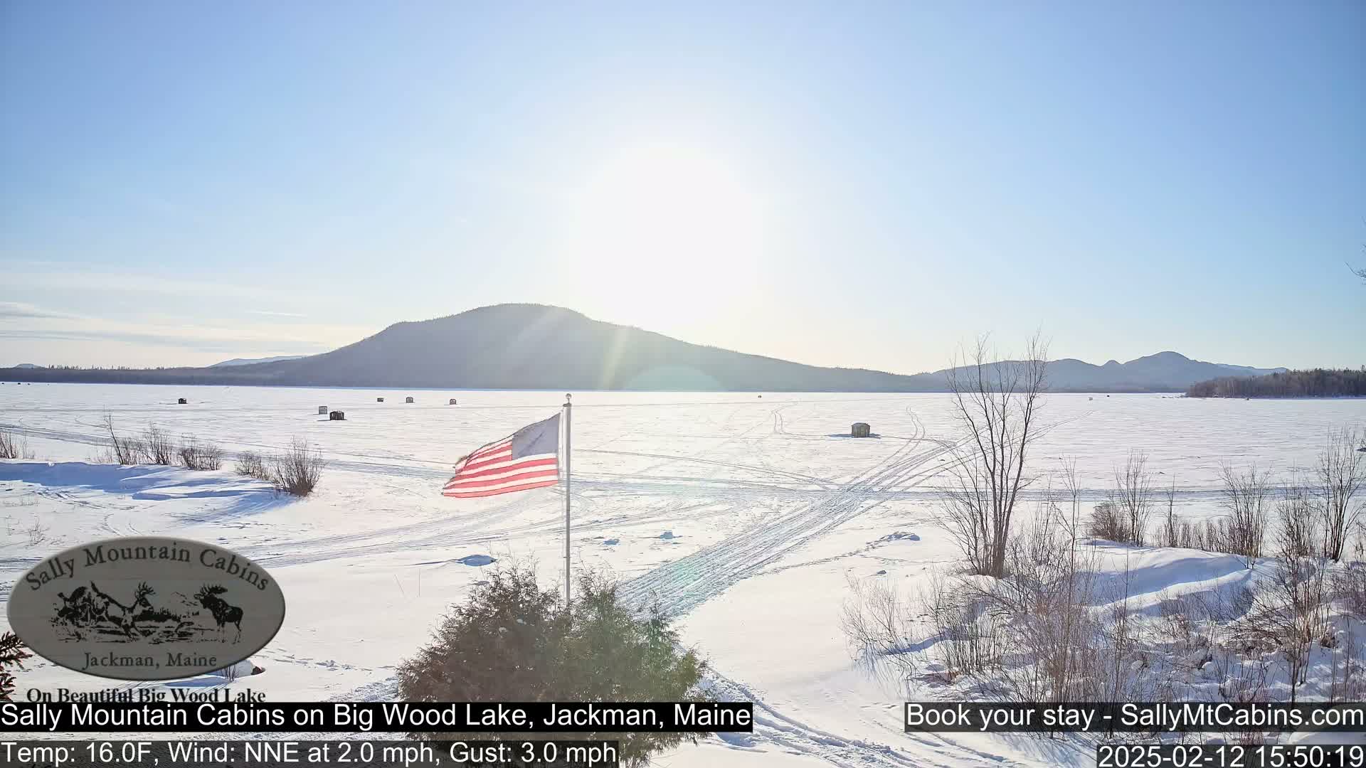 A frozen lake stretches to snow-covered mountains under a bright, sunny sky.