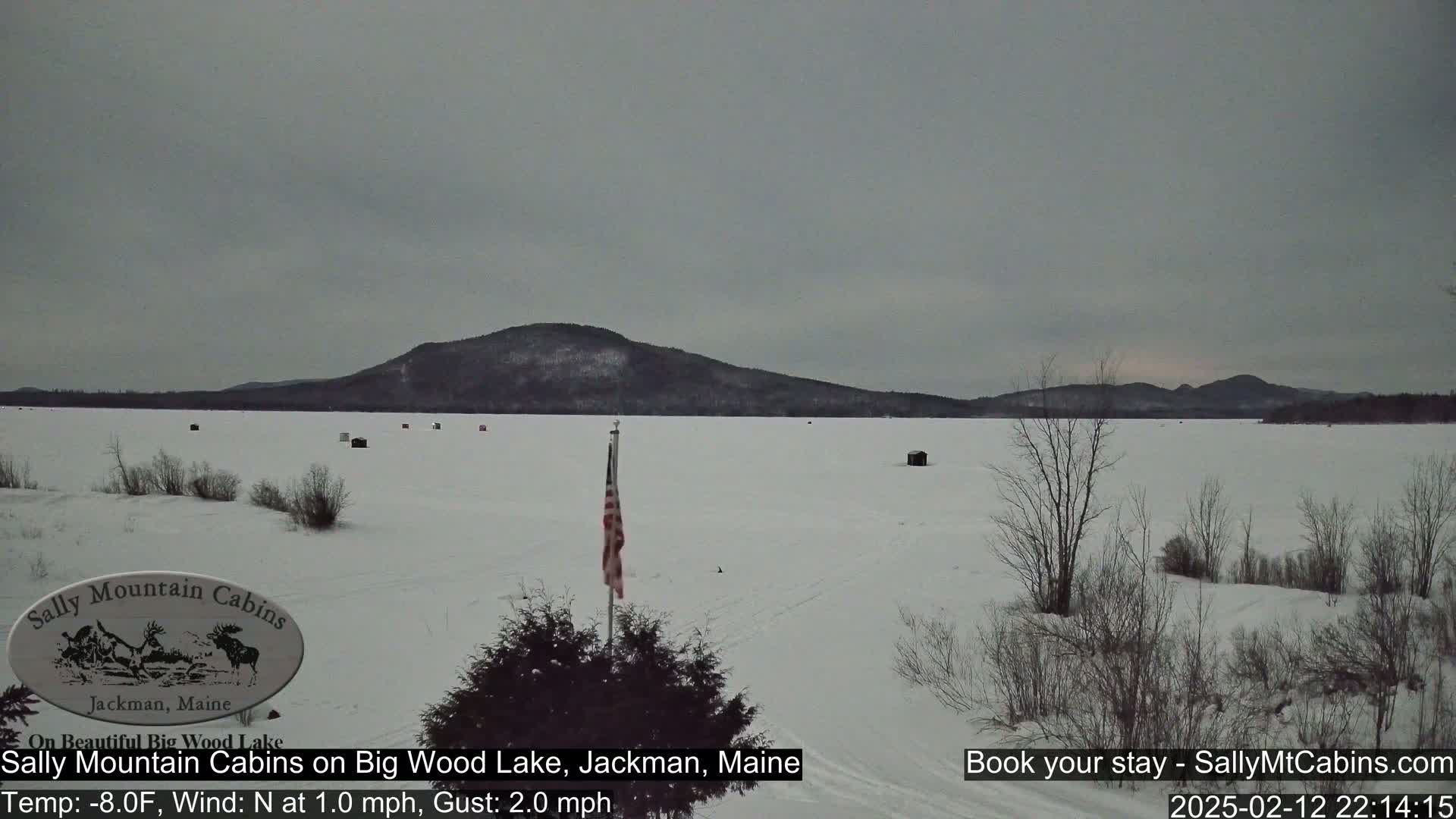 A snow-covered frozen lake stretches out before a dark, distant mountain range under an overcast sky.