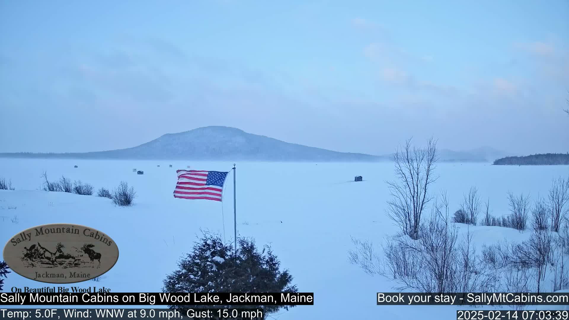 A snow-covered frozen lake with a distant mountain and a US flag flying in a cold, windy WNW breeze.