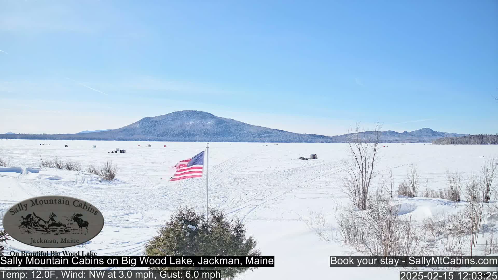 A snow-covered frozen lake stretches to a distant mountain range under a clear blue sky.