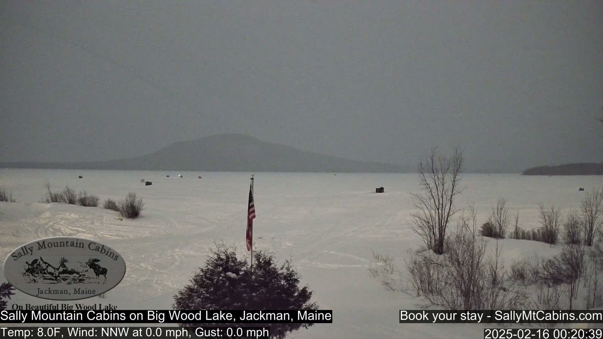 A snow-covered frozen lake stretches to a distant mountain range under a gray, overcast sky.