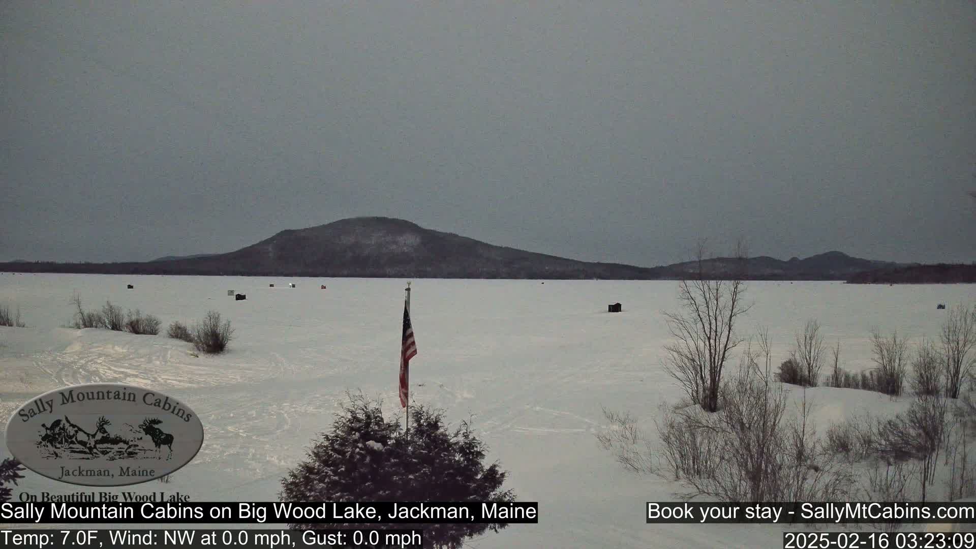 A snow-covered frozen lake stretches to a distant mountain range under an overcast sky.