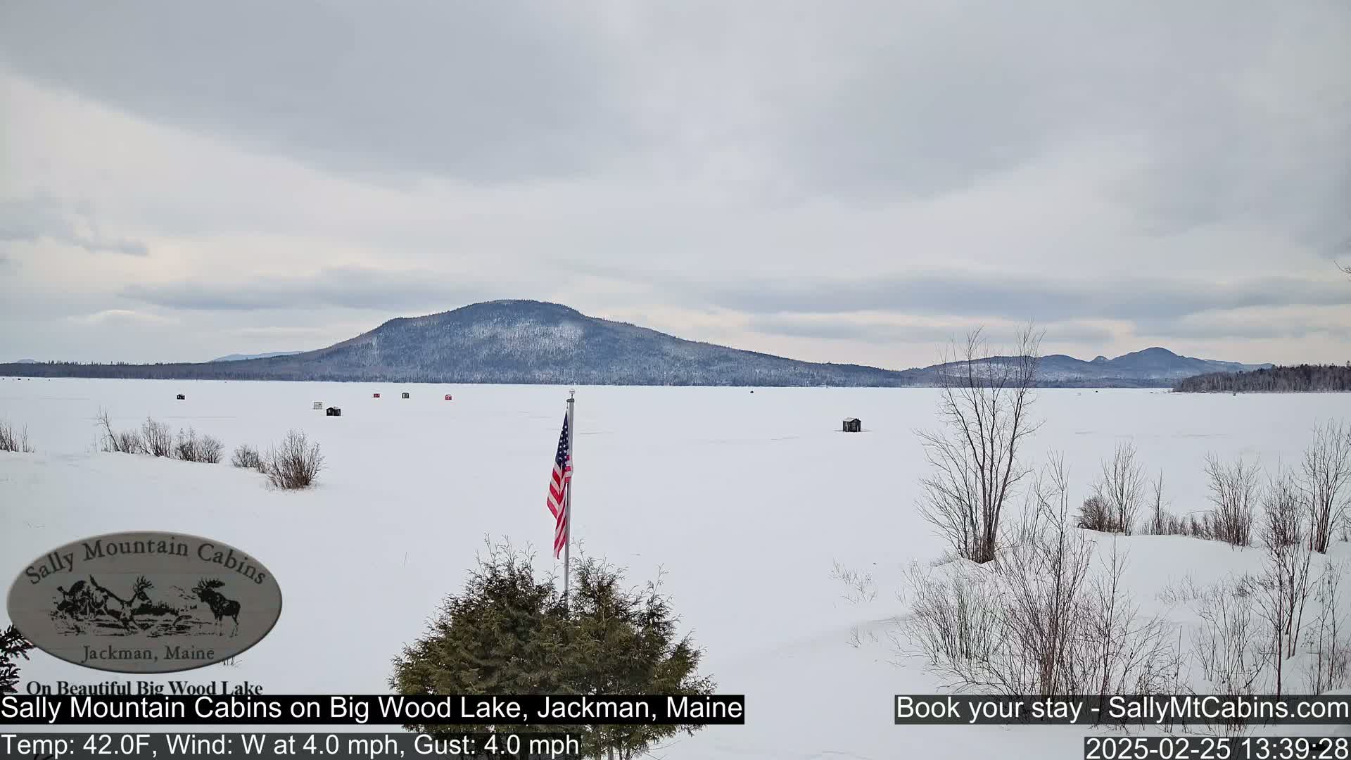 A frozen lake stretches to a distant, snow-covered mountain range under an overcast sky.