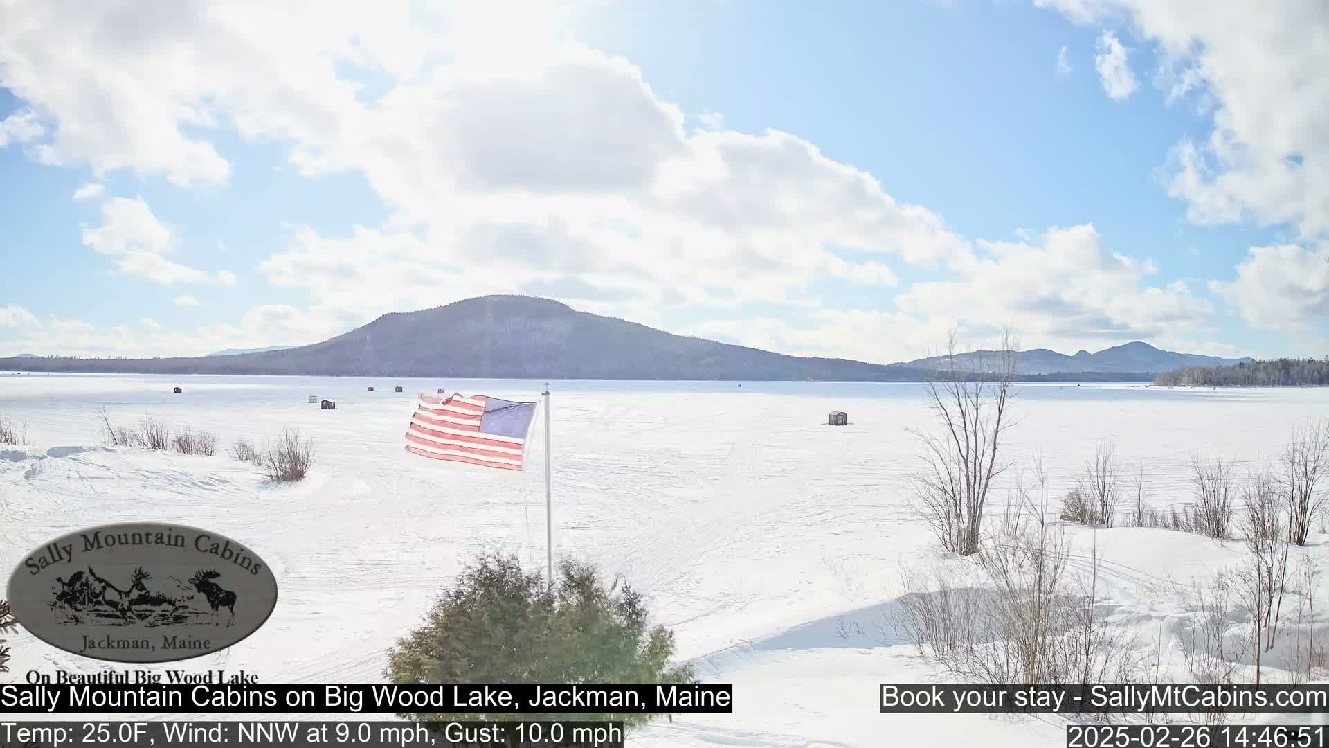 A snow-covered frozen lake stretches out before a distant mountain range under a partly cloudy sky.