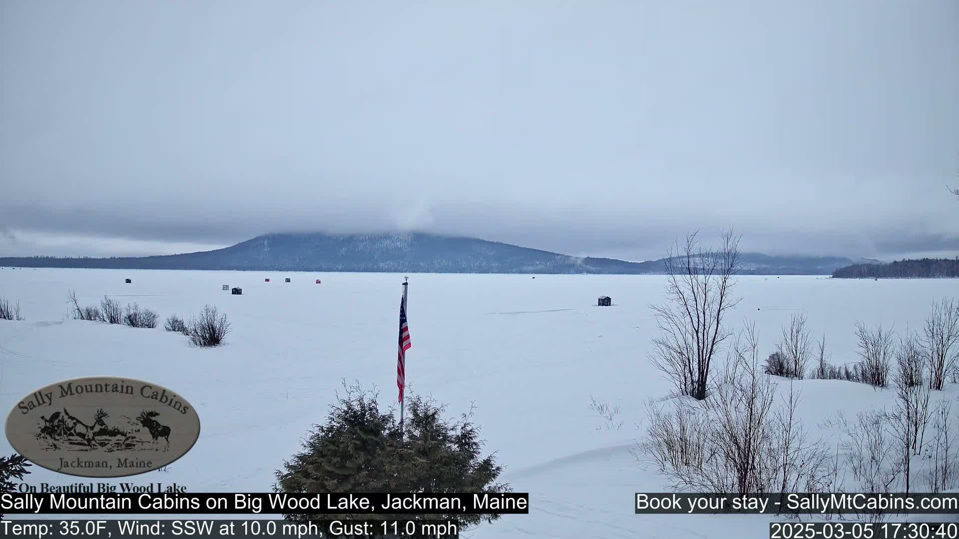 A snow-covered frozen lake stretches to a distant, low mountain range under an overcast sky.