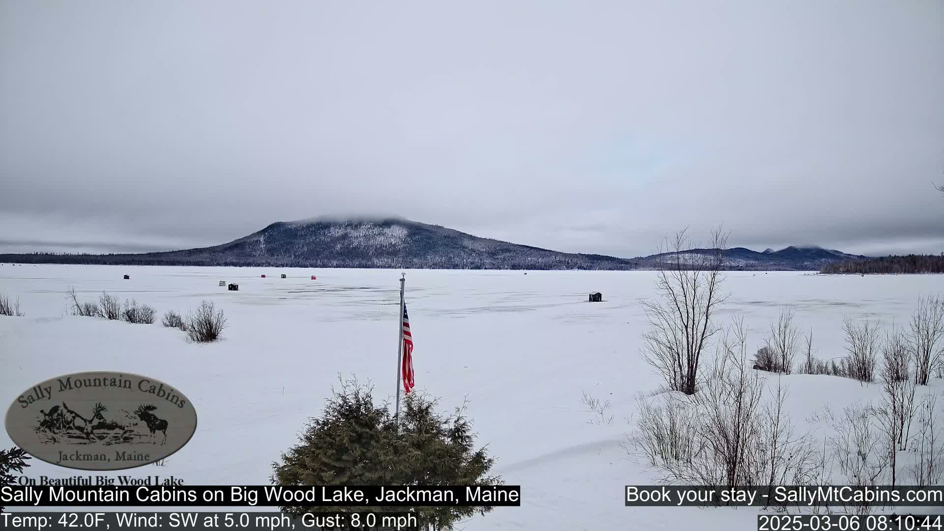 A snow-covered frozen lake stretches to a distant mountain under an overcast sky.