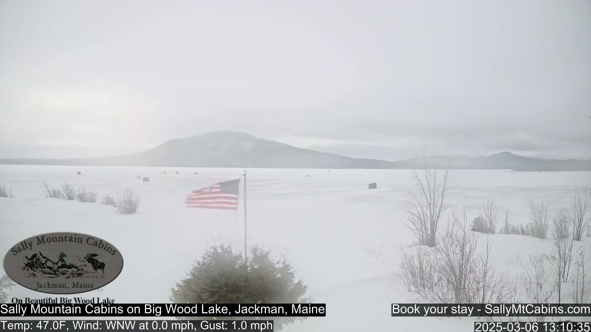 A snow-covered frozen lake stretches to a hazy mountain range under an overcast sky.