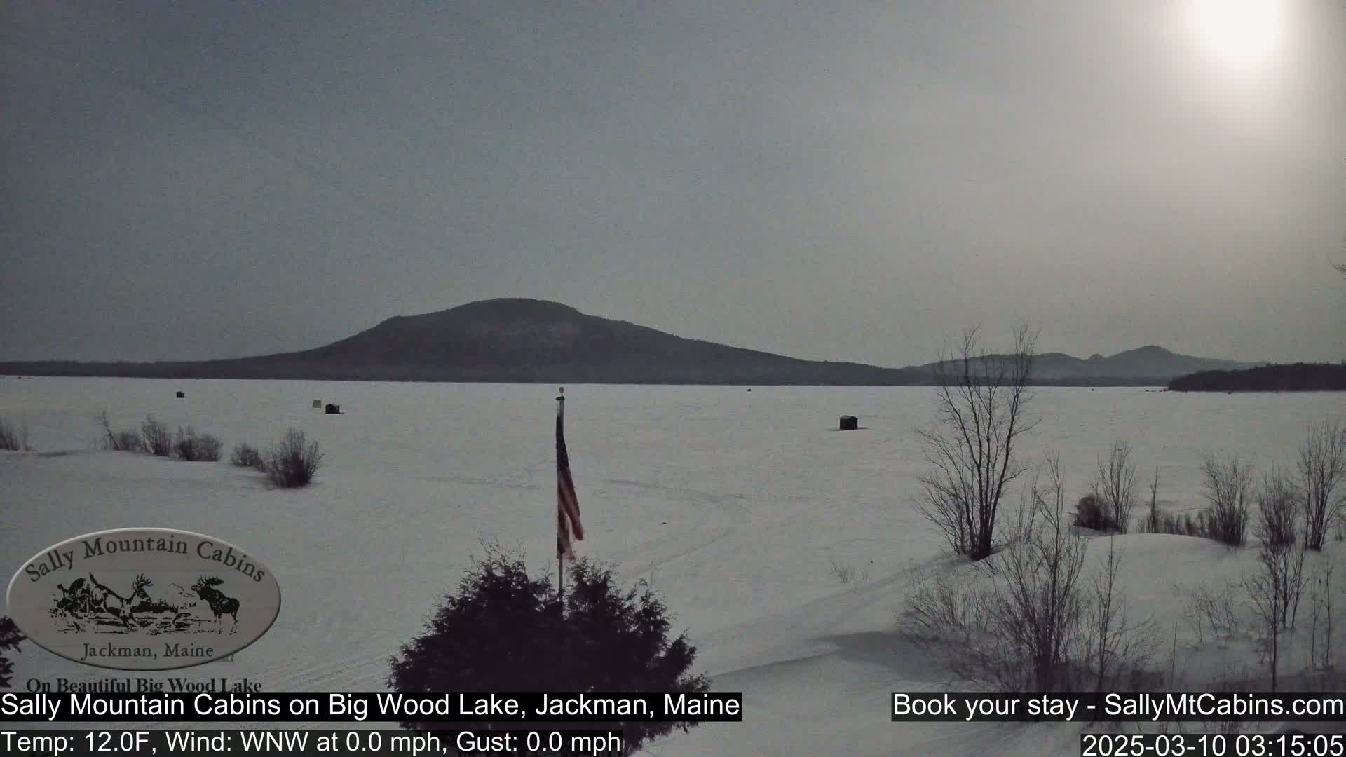 A snow-covered frozen lake stretches to a distant mountain range under a bright, overcast sky.