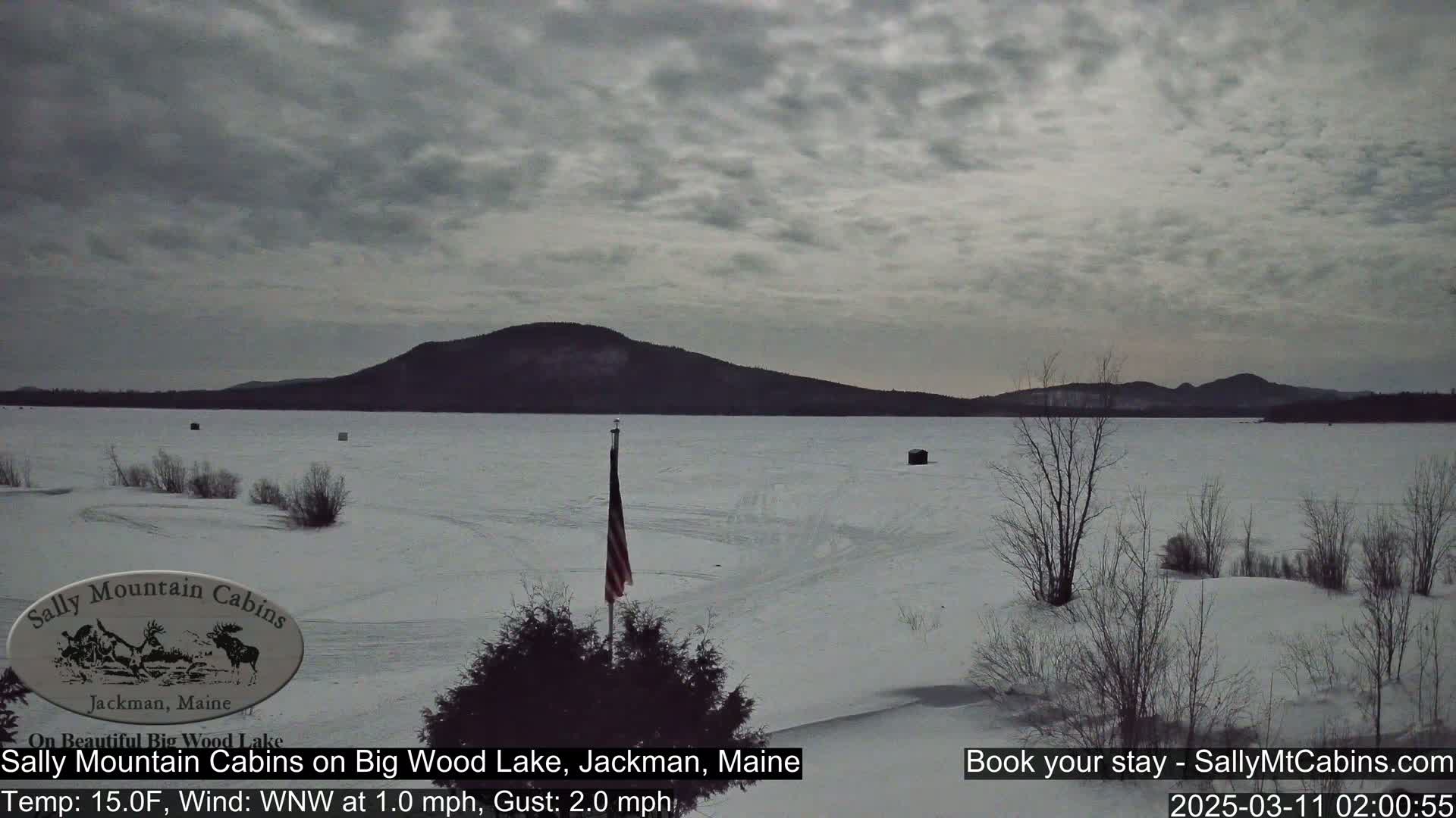 A snow-covered frozen lake stretches towards a dark mountain under a cloudy sky.