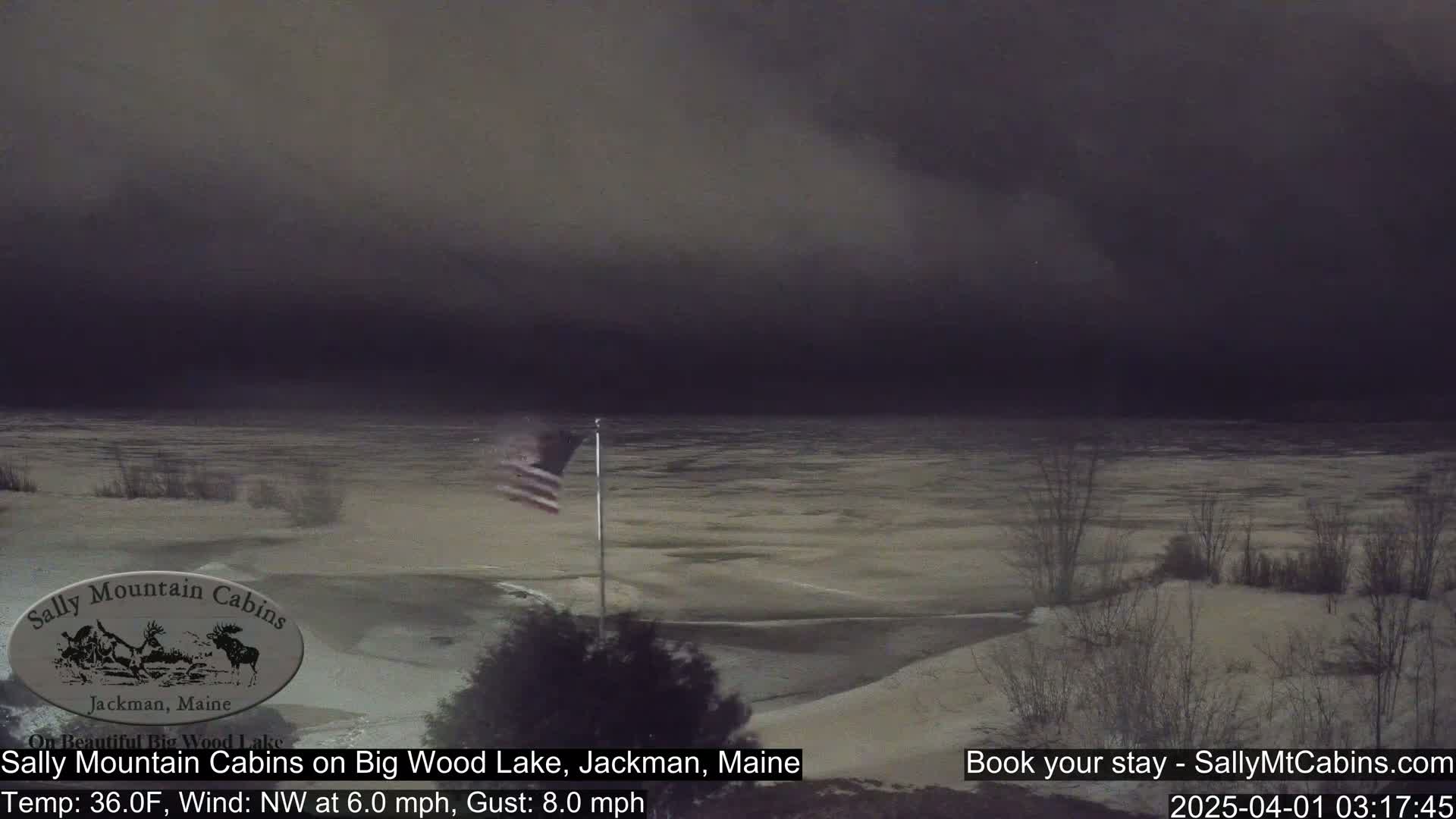 A partially frozen lake is visible under a dark, overcast sky, with a small American flag waving in the wind.