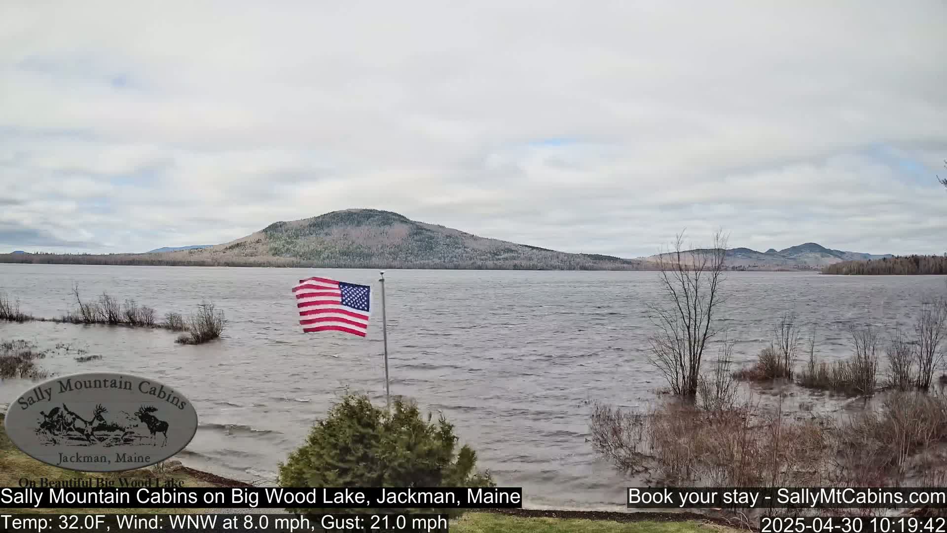 A choppy lake with a distant mountain range under an overcast sky, and an American flag waving in the wind.