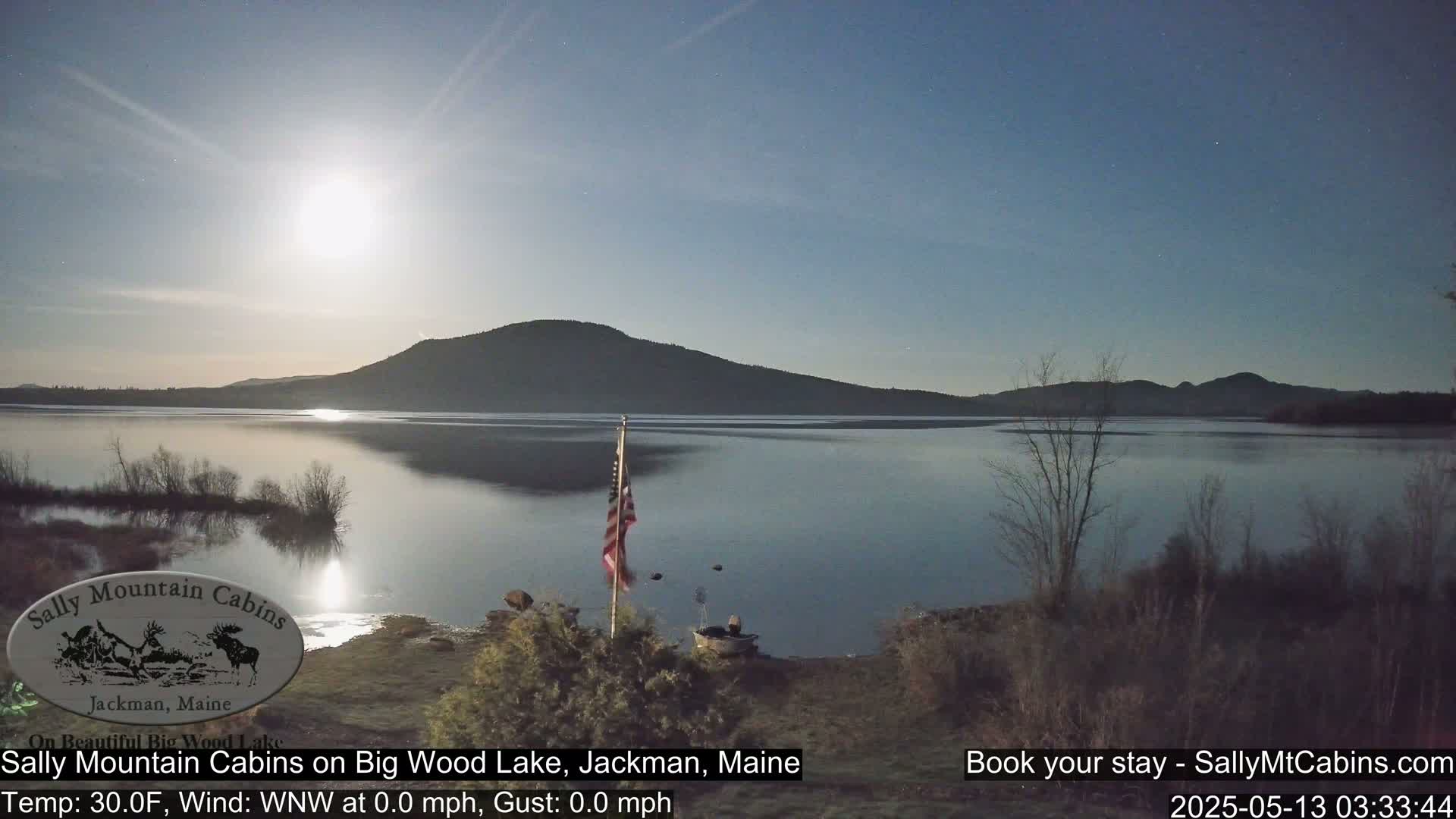 A calm, moonlit night scene shows a lake reflecting the bright moon and a distant mountain range under a clear sky.