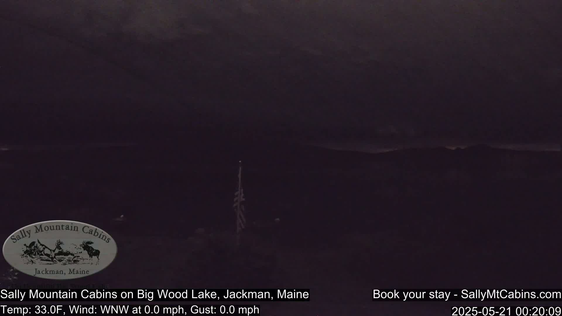 A dark, nighttime view of a lake and distant hills under a cloudy sky.