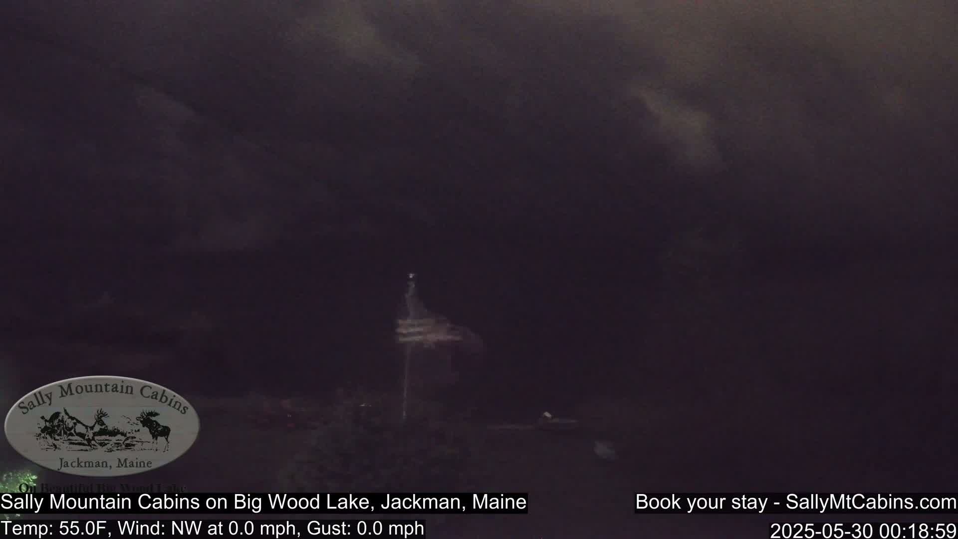A dark, overcast scene shows a dimly lit structure near a body of water under a mostly dark sky.