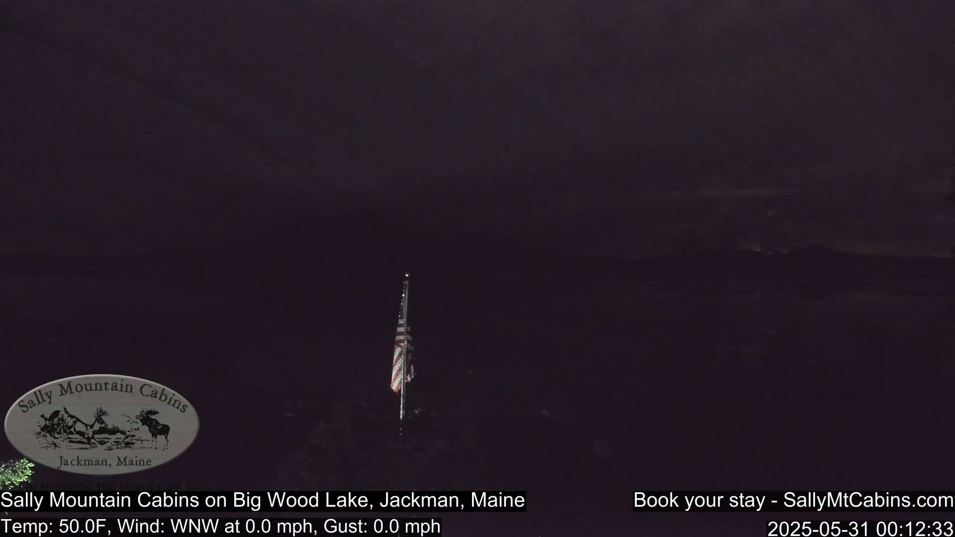 A dark, nighttime scene shows a flagpole with an American flag silhouetted against a mostly dark sky.