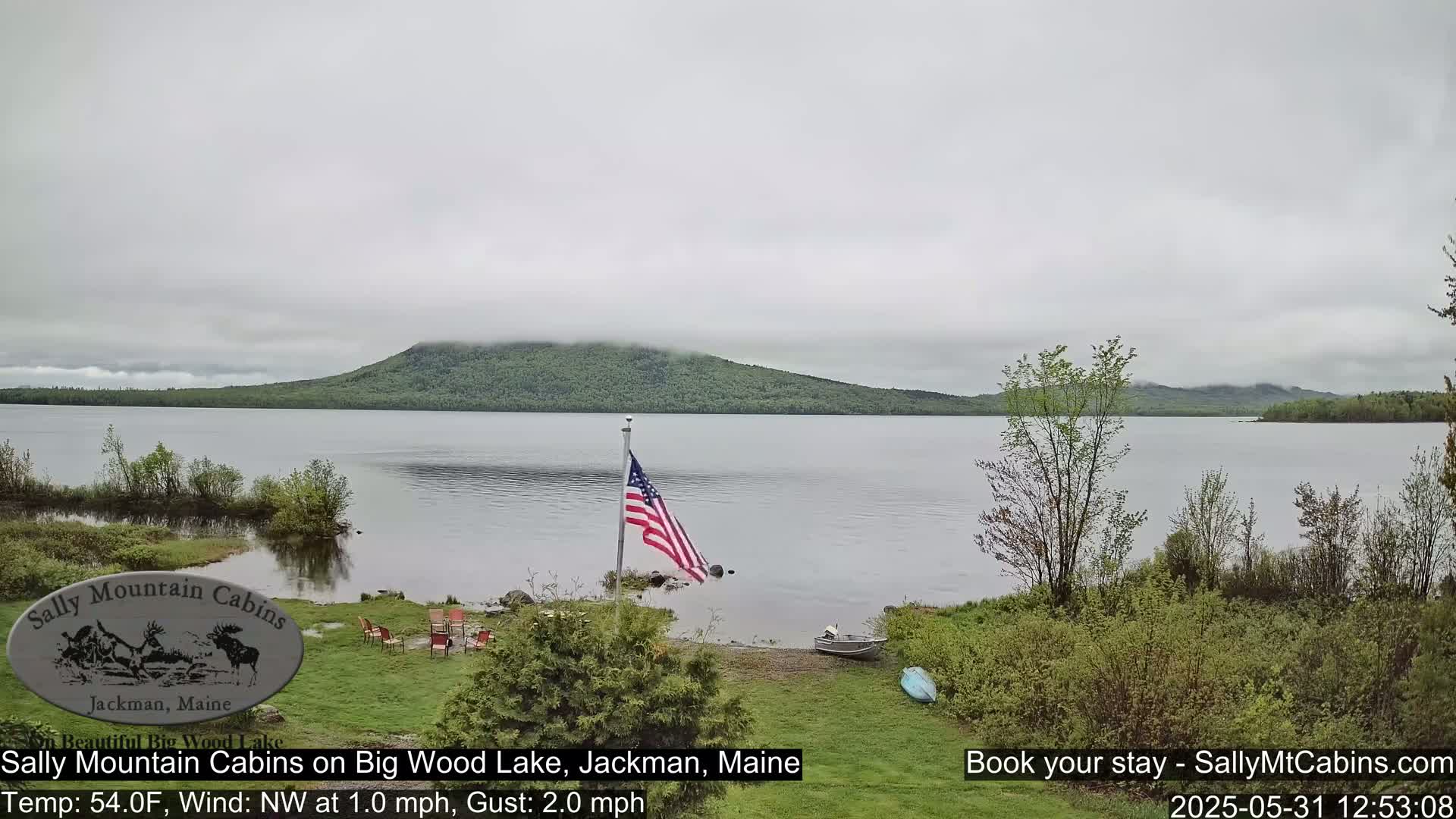A calm lake with a hazy sky is viewed from a lakeside property featuring an American flag and some outdoor furniture.