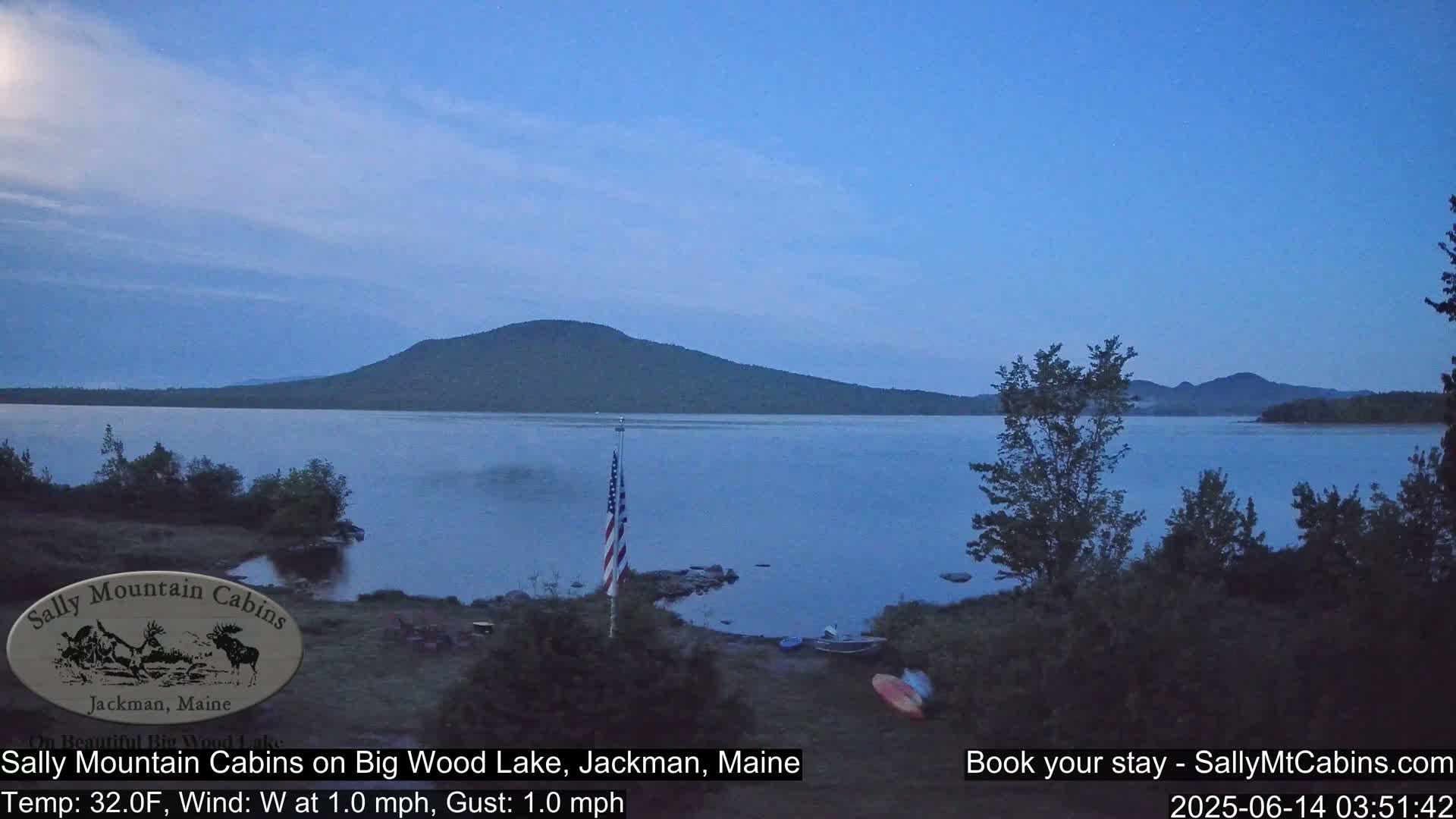 A calm, twilight view of a lake with a dark mountain in the background, under a clear, dusky sky.