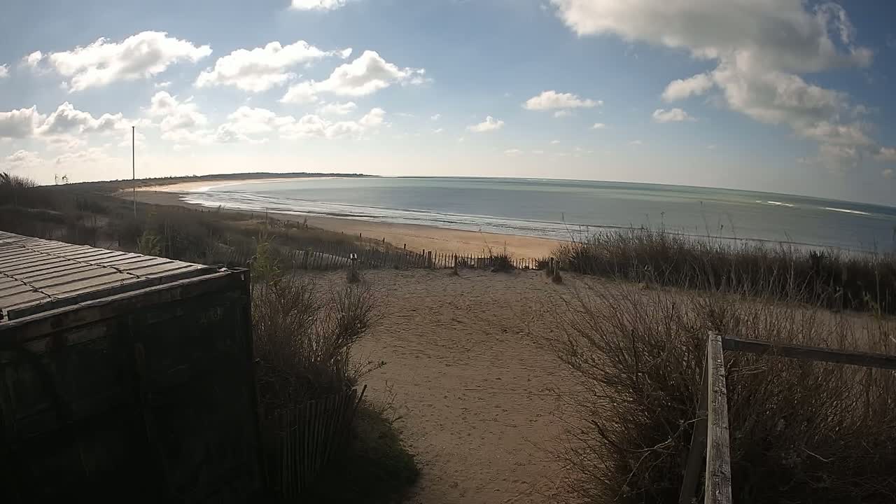 A sandy beach with a calm ocean stretches to the horizon under a partly cloudy sky.