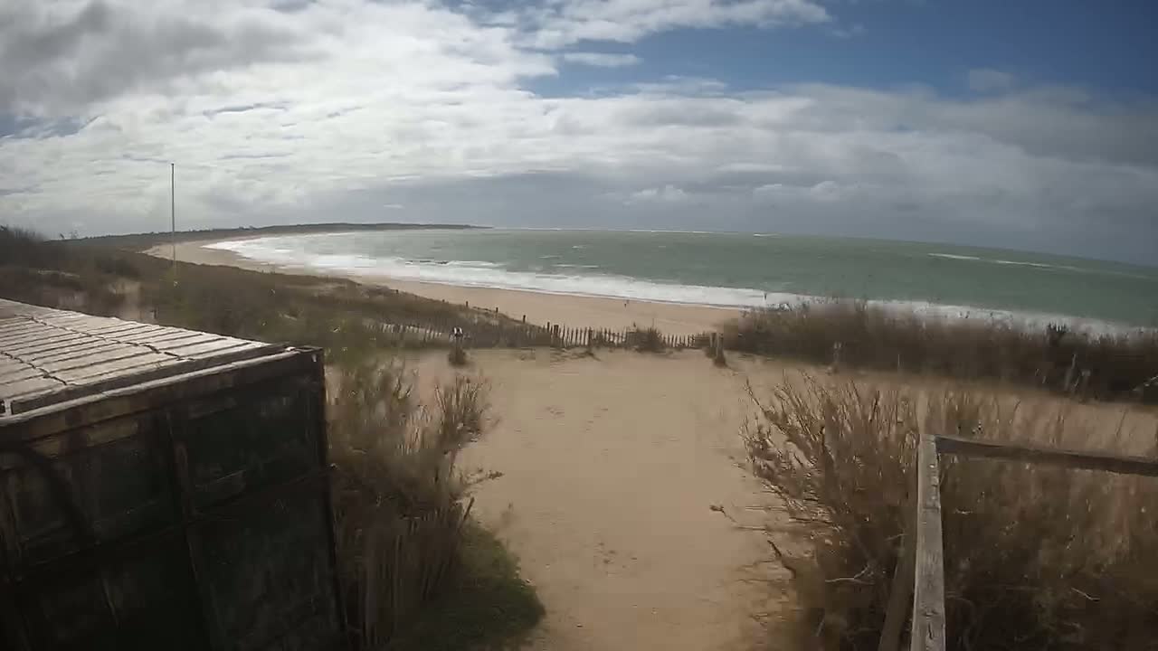 A sandy path leads down to a beach with moderate waves under a partly cloudy sky.