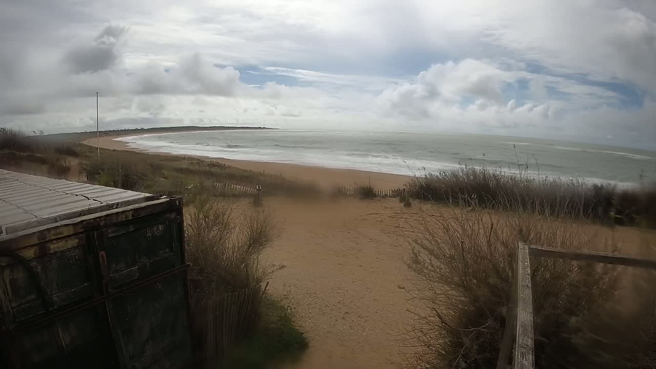 A sandy beach with a choppy ocean under a cloudy sky is seen from behind a partially visible cargo container.
