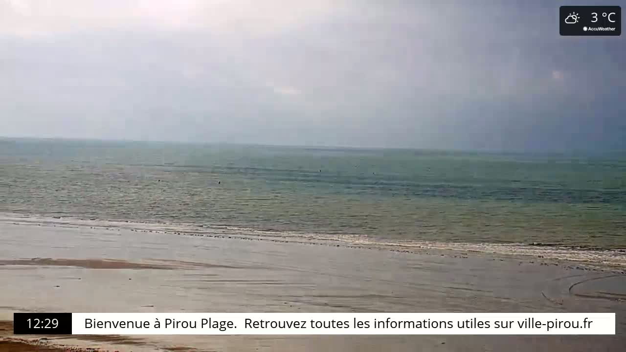 A wide shot of a calm, gray-green ocean meeting a flat, sandy beach under a cloudy sky with a temperature of 3°C.