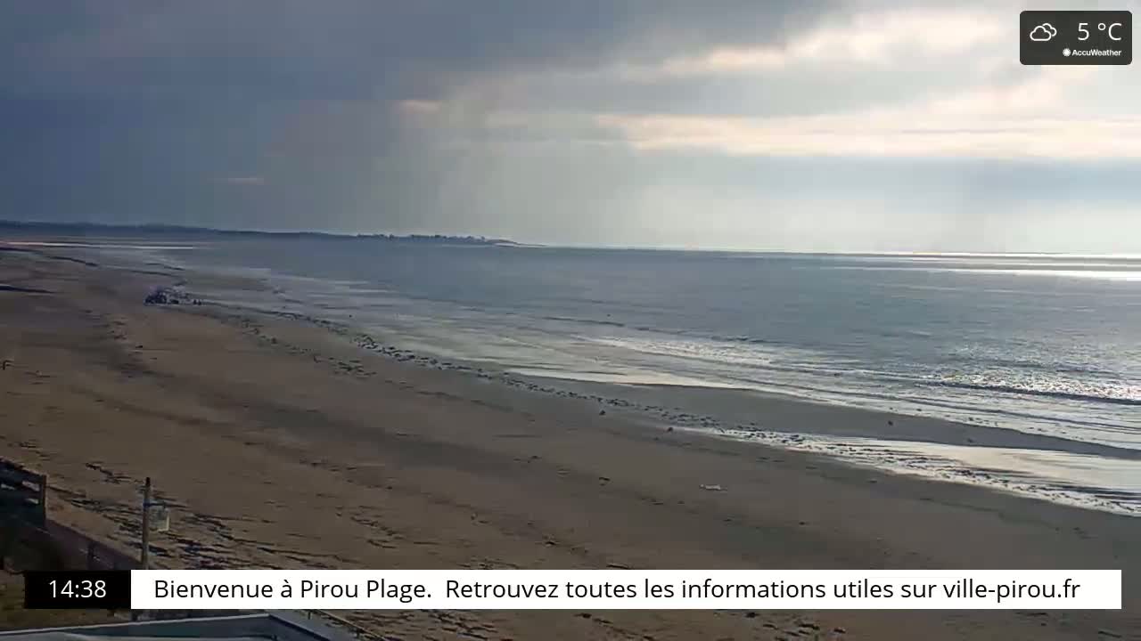 A long, sandy beach stretches to a calm ocean under a cloudy sky.