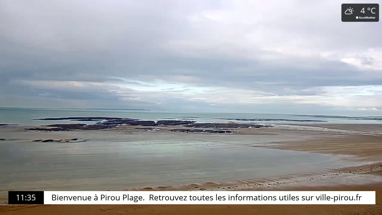 A wide, sandy beach stretches towards a calm sea under a cloudy sky.