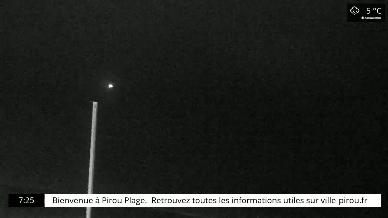 A tall, thin light pole stands in the dark under a slightly overcast night sky.