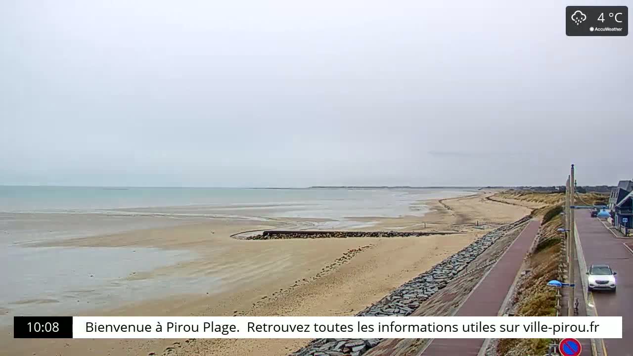 A wide sandy beach stretches along a calm, light-grey ocean under an overcast sky.