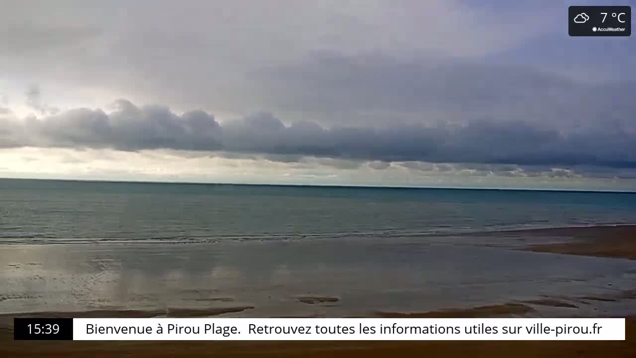 A calm ocean meets a sandy beach under a cloudy, 7°C sky.