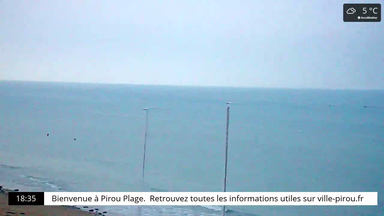 A calm, overcast ocean scene at 5°C shows a sandy beach with three tall poles extending from the shore into the water.
