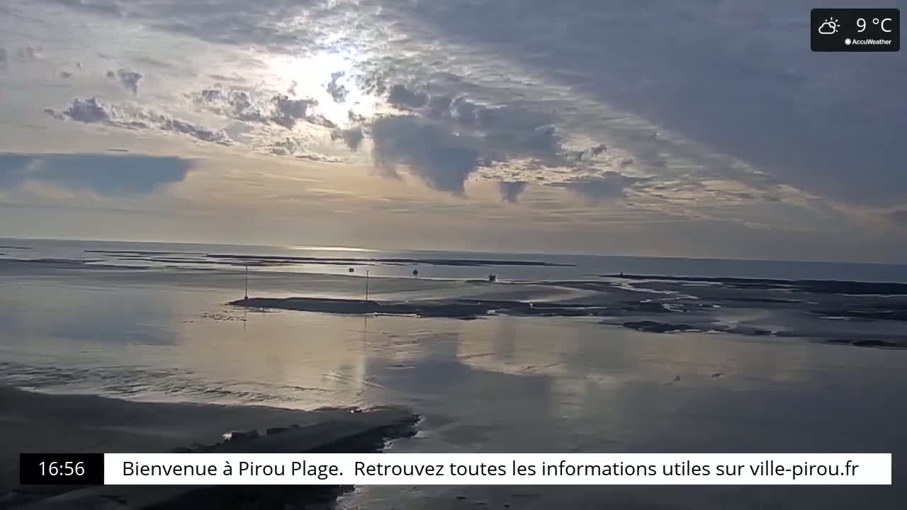 A partly cloudy sunset over a calm, shallow body of water at low tide, with a small landmass in the middle distance.