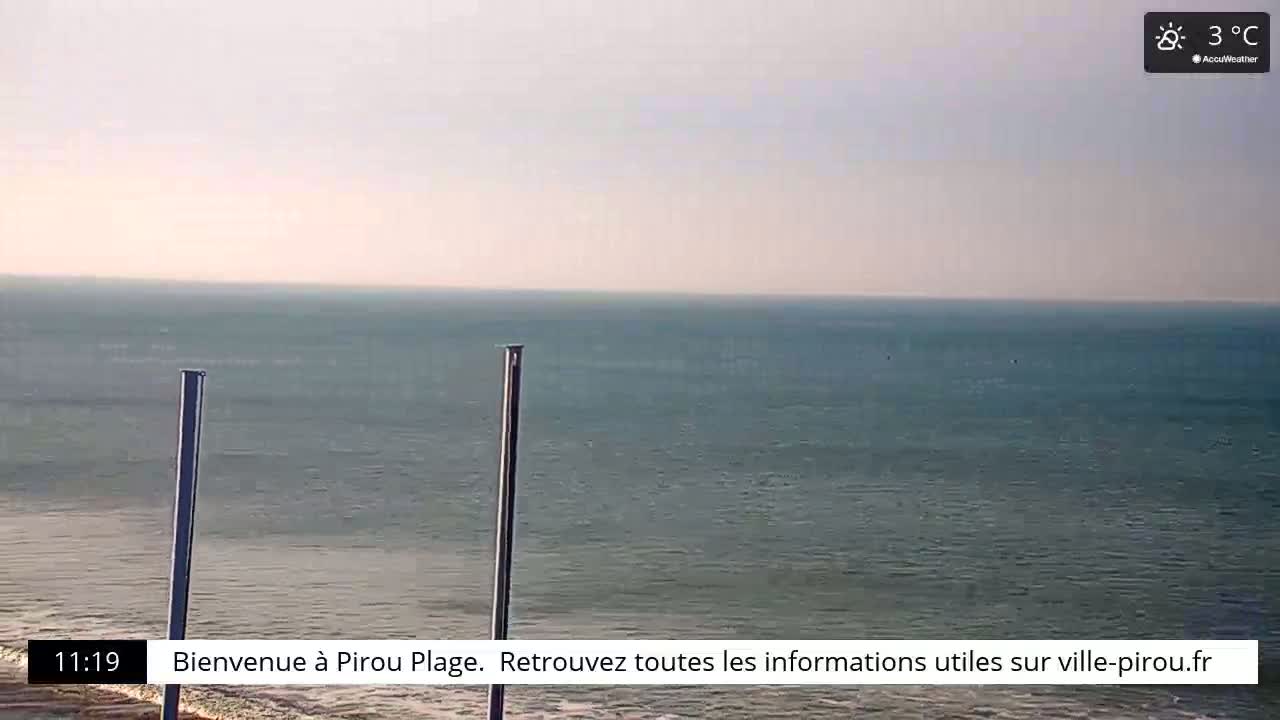 A calm, teal ocean is visible under a hazy, light-pink sky, with two tall, thin posts in the foreground; the temperature is 3°C.
