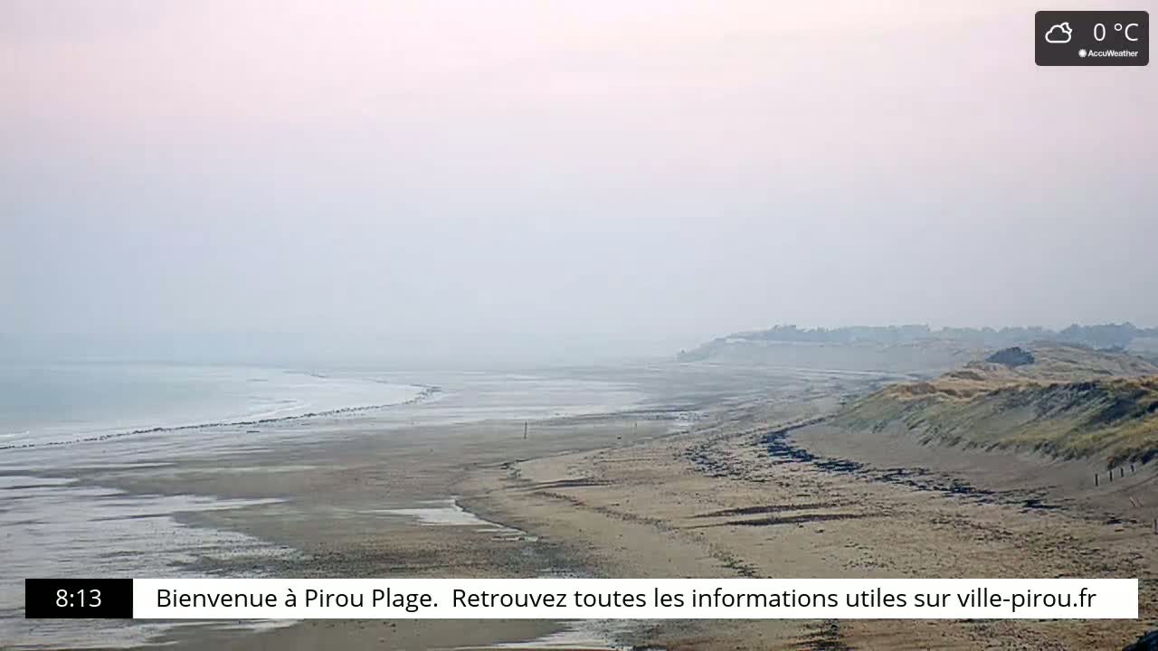 A hazy, sandy beach stretches along a calm sea under a cloudy, 0°C sky.