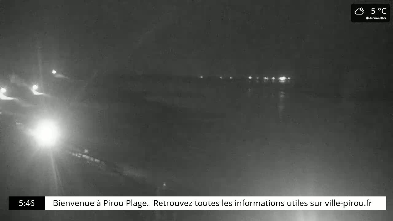 A nighttime, low-light view of a dark body of water with a few lights visible in the distance, under cloudy skies at 5°C.