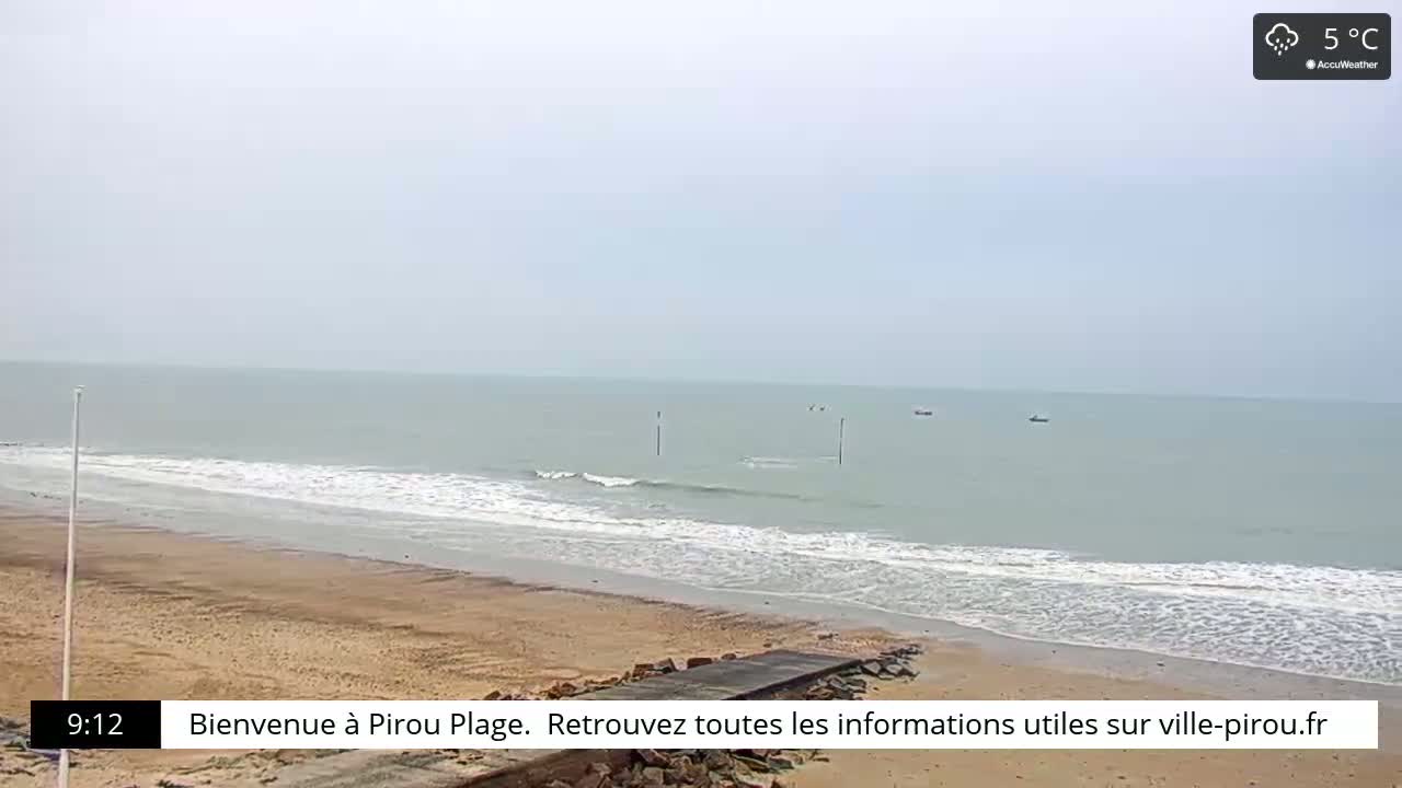 A sandy beach meets a calm, light-green sea under an overcast sky.