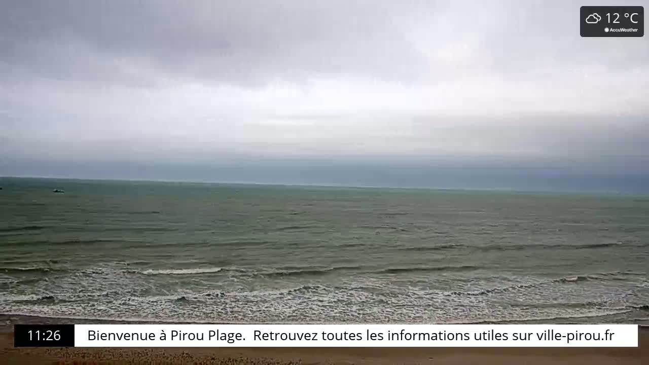 A wide shot of a grey, overcast beach scene shows a calm sea with small waves lapping a sandy shore under a cloudy sky.