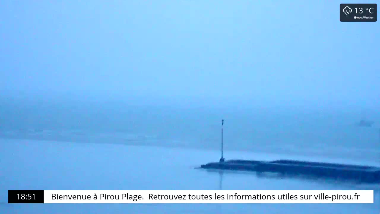 A hazy, light blue body of water is shown, with a dark structure partially submerged in the water in the foreground.