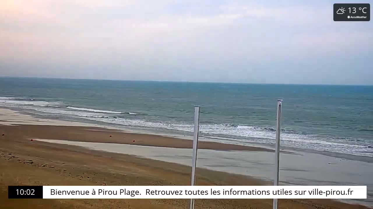 A wide sandy beach with gentle waves rolling onto the shore under a cloudy sky.