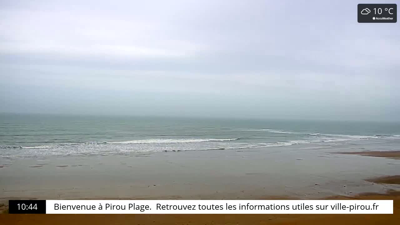 A wide shot of a beach with calm, grey-green ocean waves under an overcast sky.