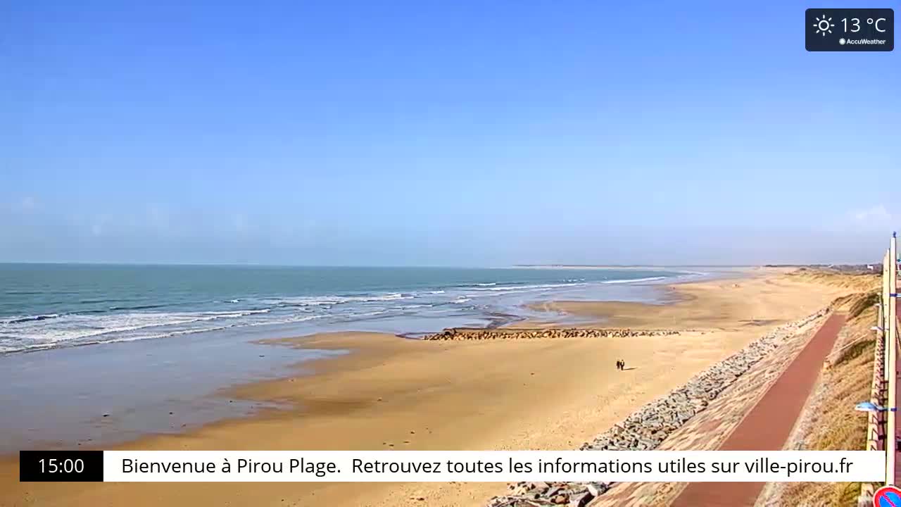 A wide sandy beach with gentle waves under a clear blue sky stretches to a calm ocean.