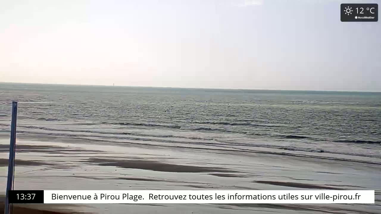 A wide shot of an ocean beach on a sunny, 12°C day shows gently rolling waves lapping a long, wide, sandy shore.