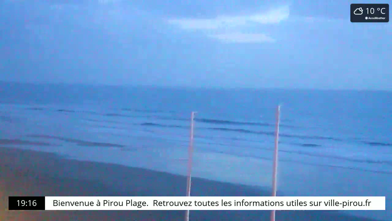 A mostly cloudy sky overlooks a calm ocean with small waves gently lapping a sandy beach, the air temperature is 10°C.
