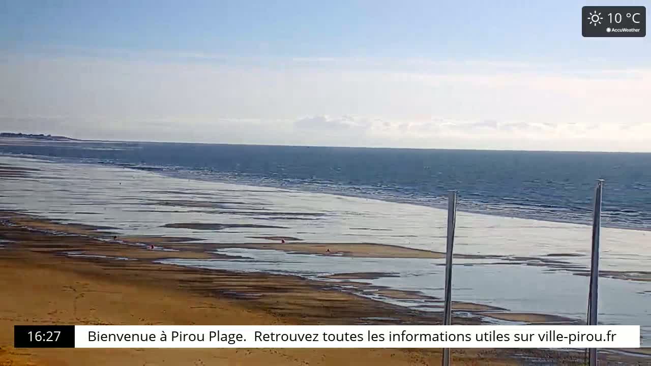 A wide sandy beach with scattered puddles of water stretches toward a calm ocean under a mostly clear sky.