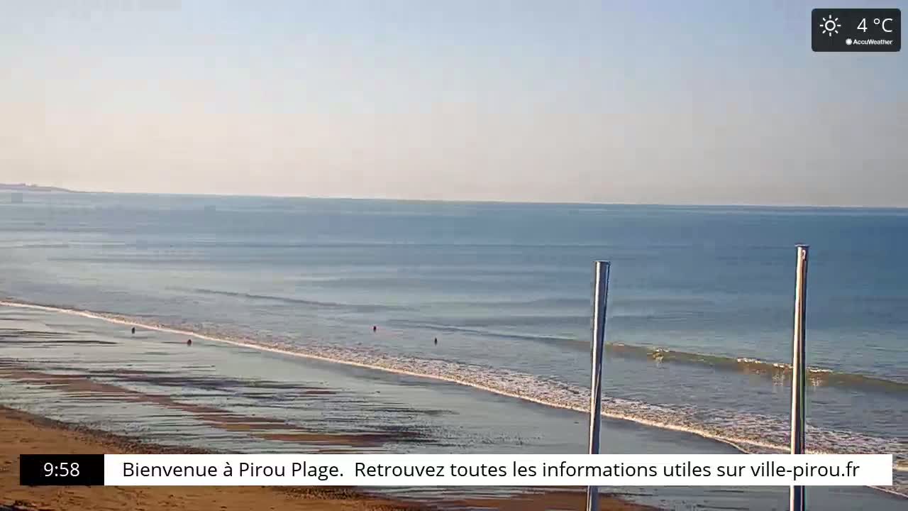 A wide sandy beach meets a calm, blue ocean under a sunny, clear sky.
