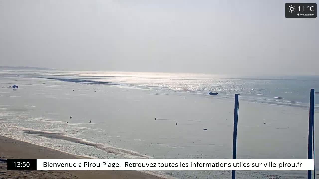 A mostly sunny beach scene shows a calm, wide expanse of water at low tide with a few small boats and a sandy shore.