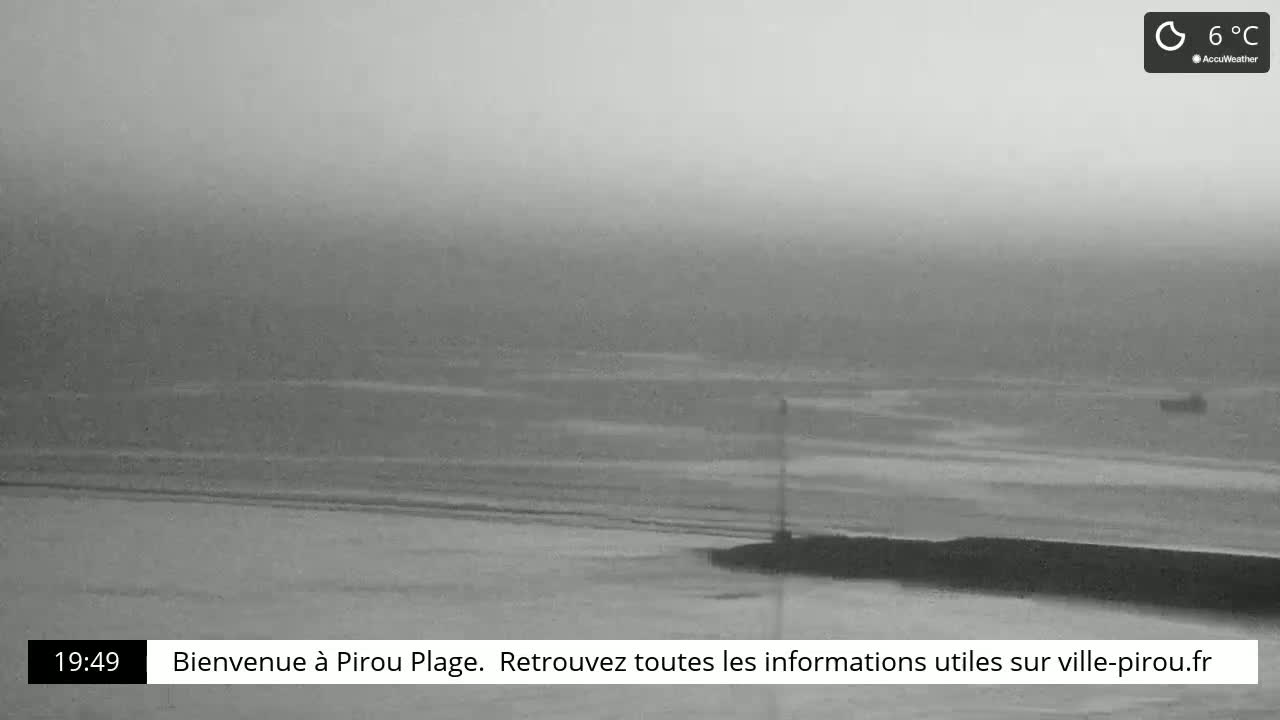 A hazy, overcast view of a calm ocean meeting a dark shoreline, with a single distant object visible on the water.
