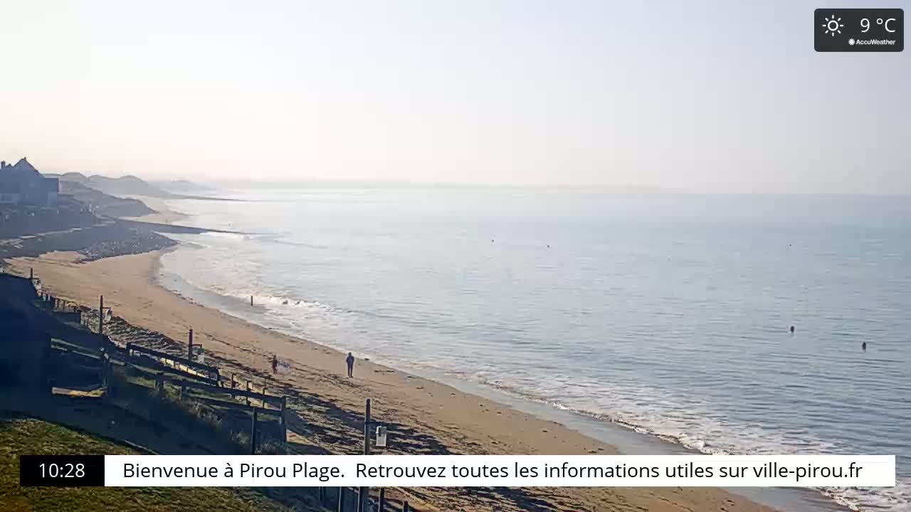 A sandy beach stretches along a calm ocean under a sunny sky.