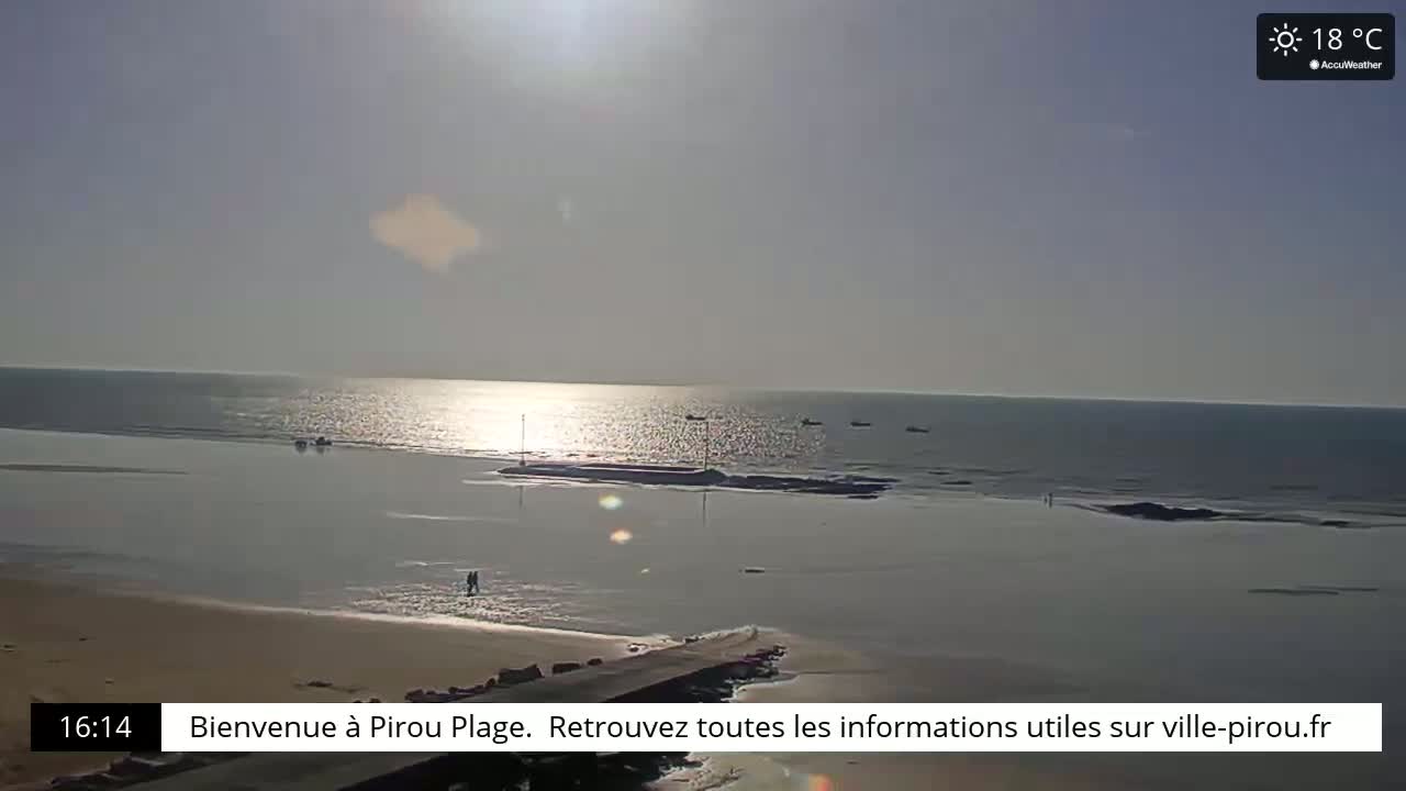 A sunny beach scene shows a calm ocean with a few boats and people walking on the sand at low tide.